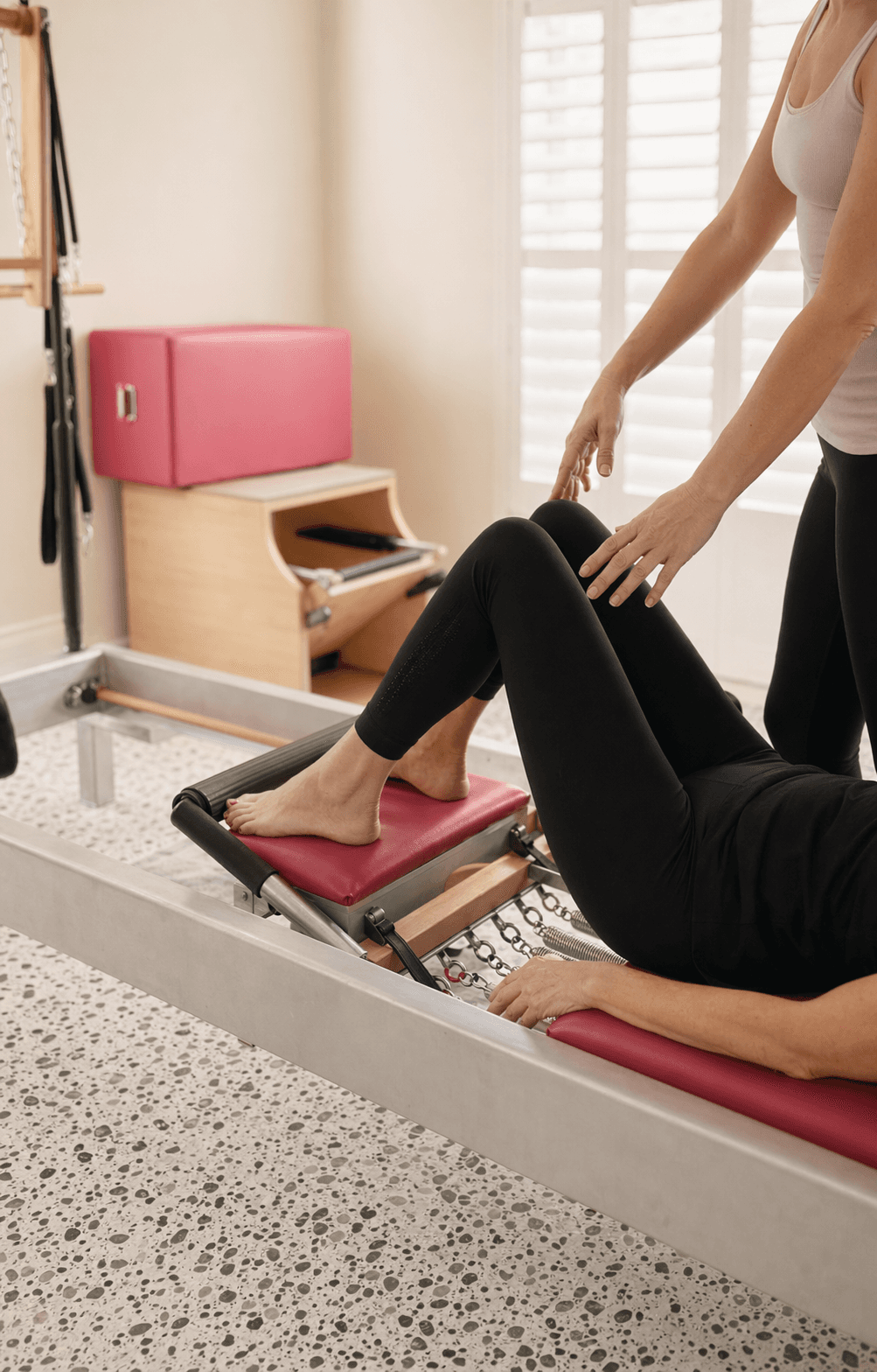Private Pilates instruction with hands guiding alignment on a reformer